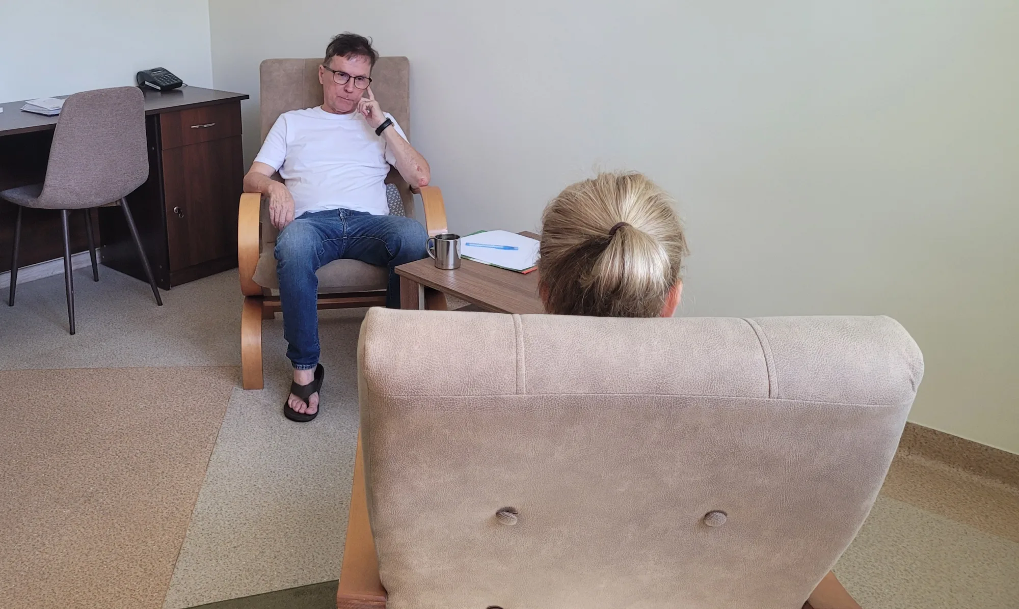 Sesja psychoterapii: terapeuta w fotelu słucha osoby siedzącej tyłem do obiektywu