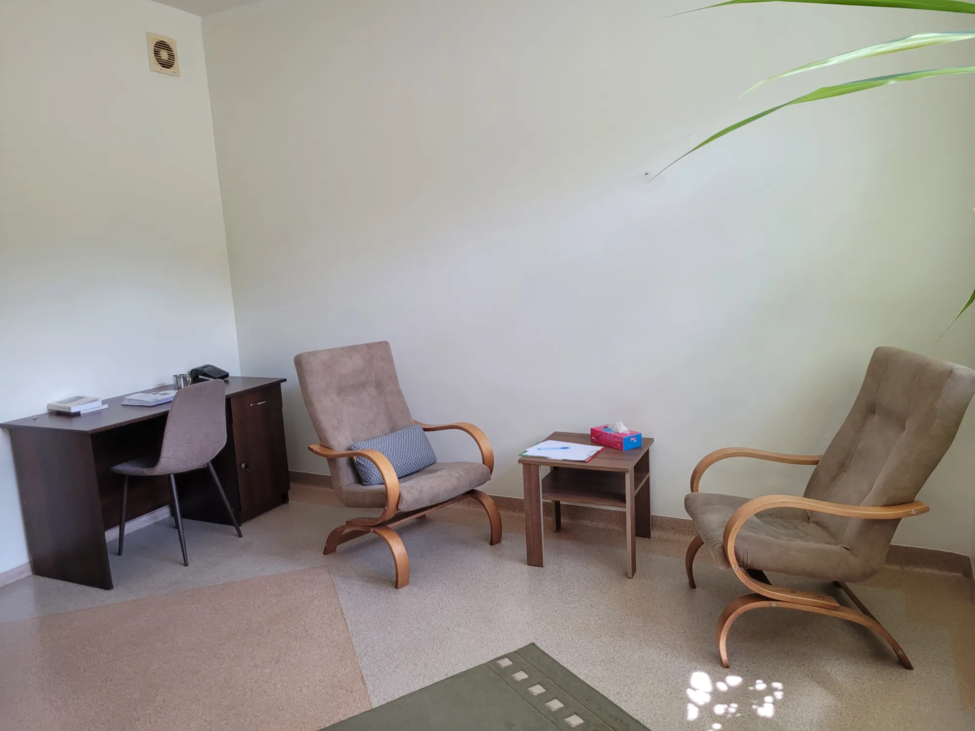 Dwa fotele ustawione naprzeciw siebie przy stoliku, w tle biurko terapeuty